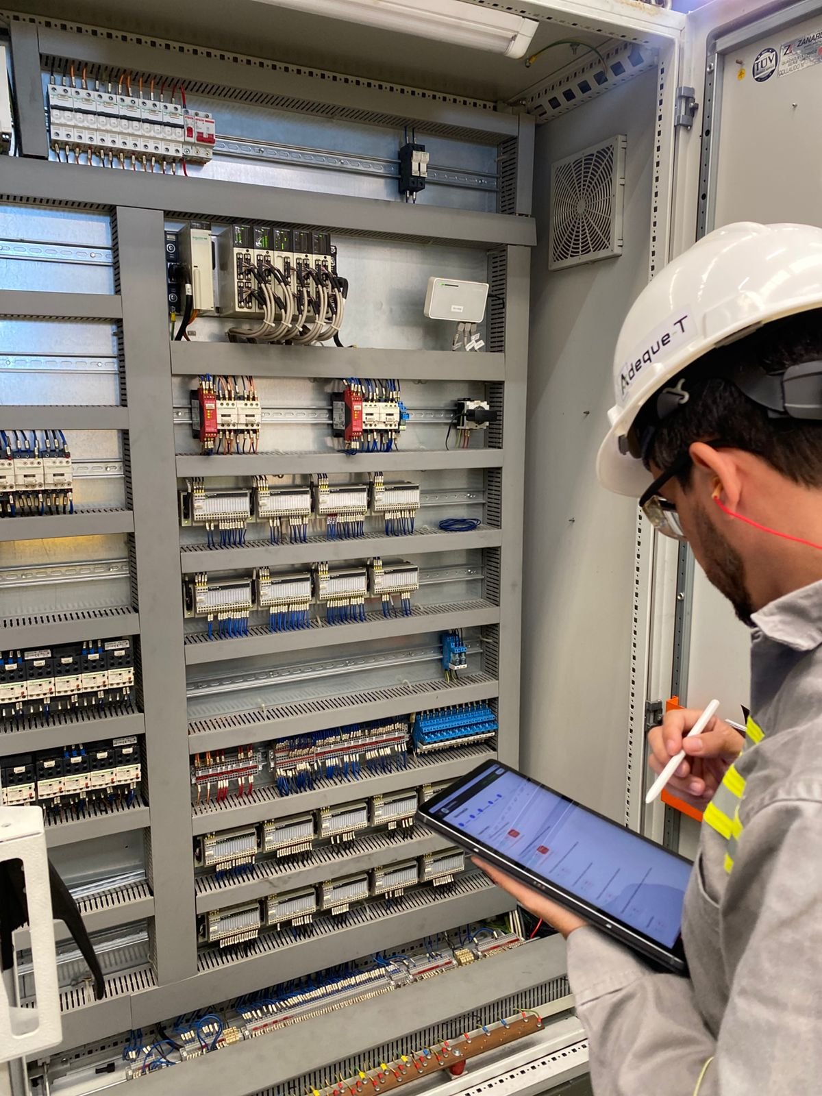 Engenheiro da Adeque-T inspecionando painel elétrico industrial com tablet