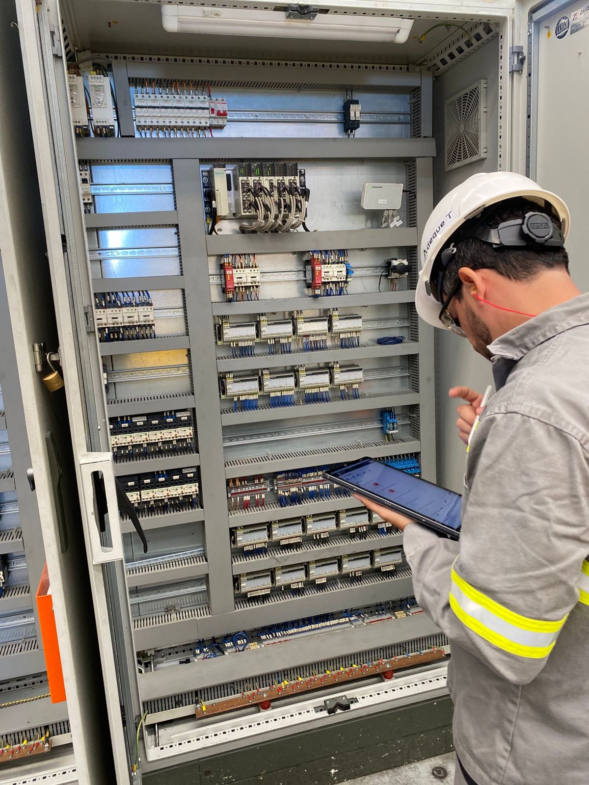 Engenheiro da Adeque-T analisando painel elétrico industrial com apoio de tablet